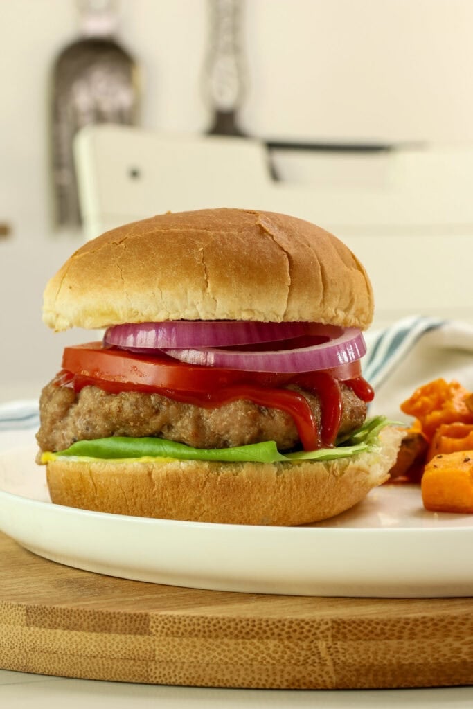 Closeup side view of a turkey burger on a bun with lettuce, tomato, red onion, and condiments.