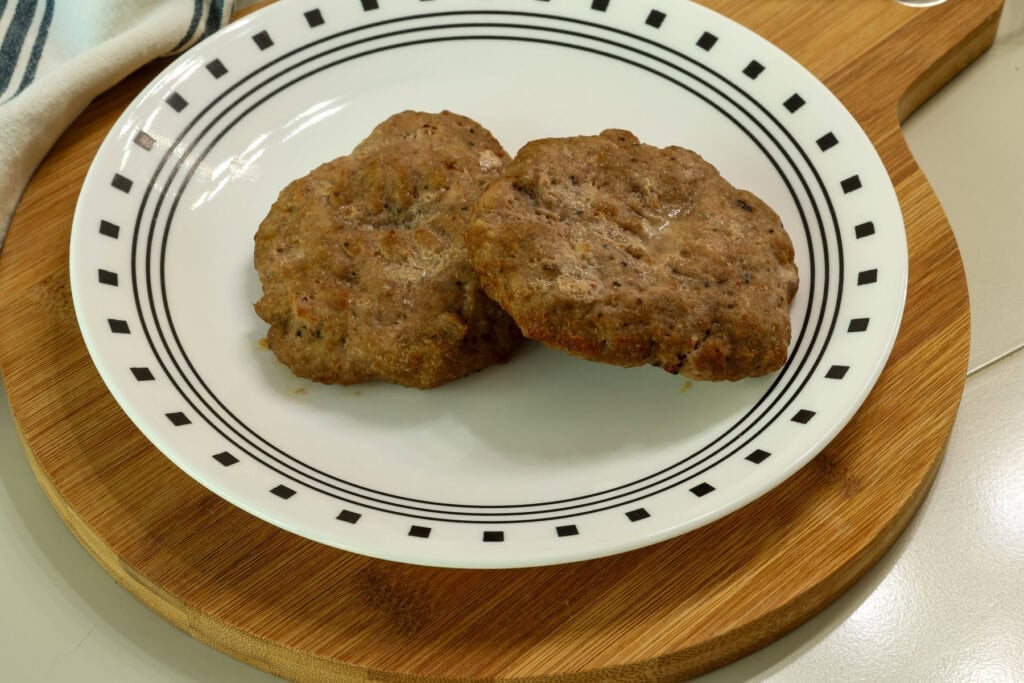 Two cooked air fried turkey burger patties on a white plate.