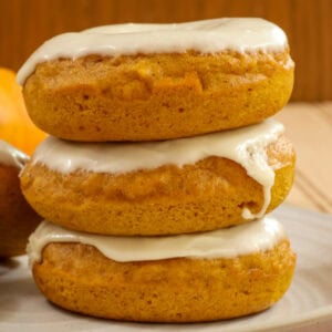 Closeup side view of three baked pumpkin donuts with maple icing stacked on top of each other.