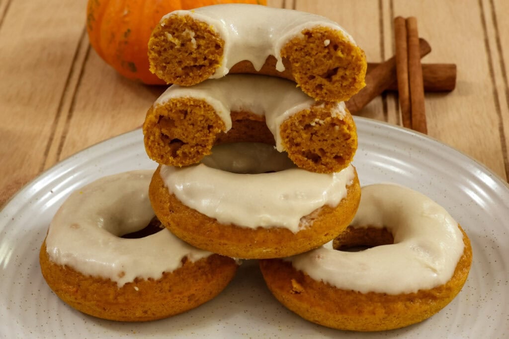 Two baked pumpkin donuts stacked on top of two donuts with one cut in half so the inside can be seen.