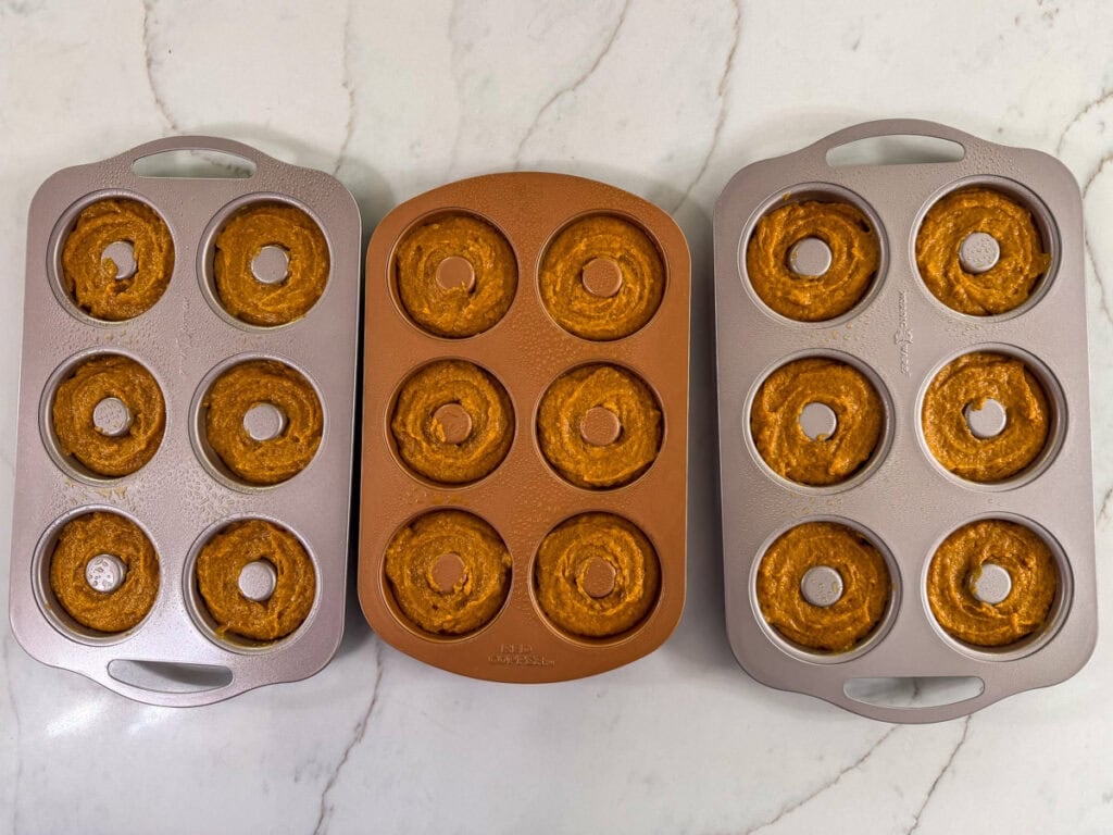Three six well donut pans filled with the pumpkin donut batter.