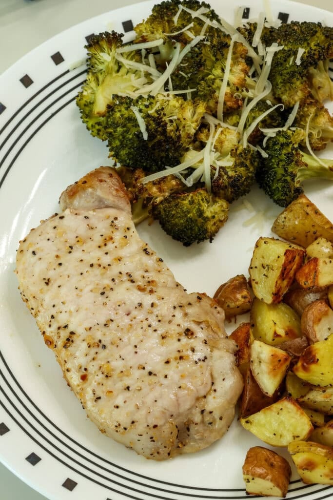Closeup overhead of a pork chop on a plate with broccoli and roasted potatoes.