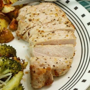Side closeup of a sliced air fried pork chop on a plate with side dishes.