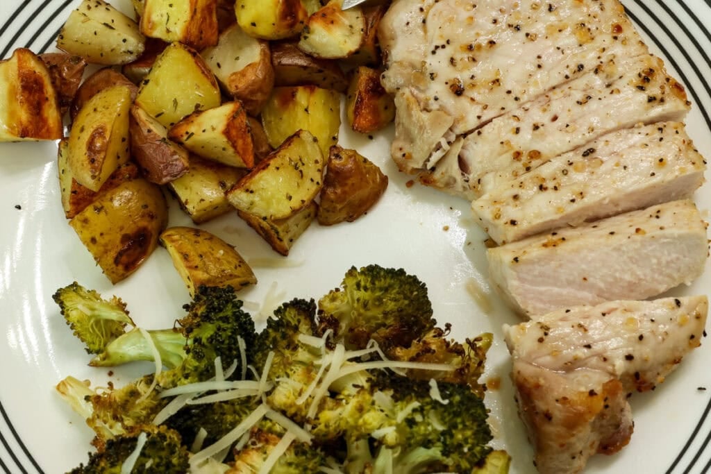 Overhead shot of a sliced air fryer pork chop on a plate with roasted broccoli and potatoes.