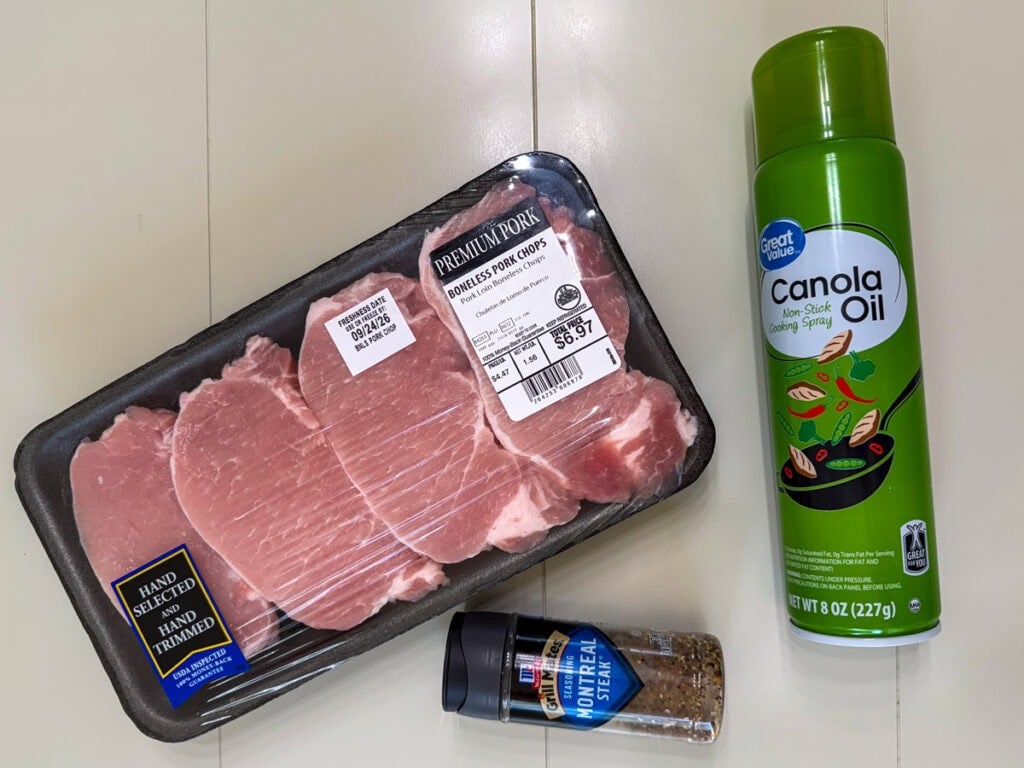 Overhead of a package of boneless pork chops, a can of nonstick canola oil spray and a bottle of Montreal steak seasoning.