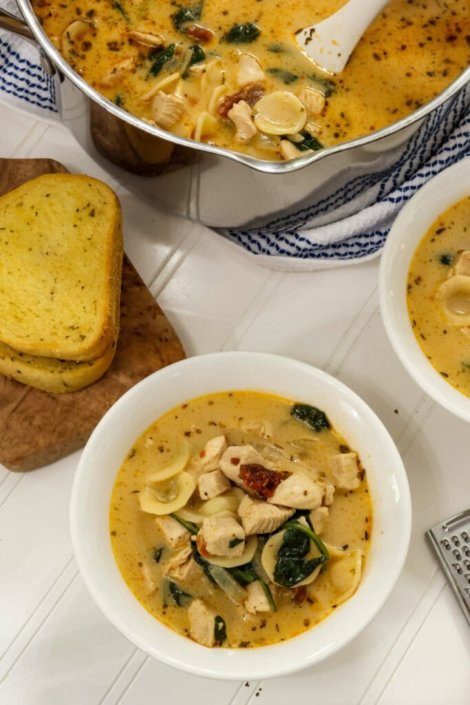 One bowl of Marry Me Chicken Soup and another bowl, the pot of soup, and a couple of pieces of garlic bread are partially visible.