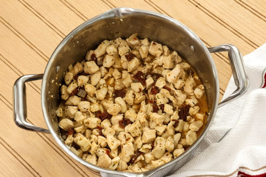 The cooked chicken in a large pot with seasonings and sun dried tomatoes.