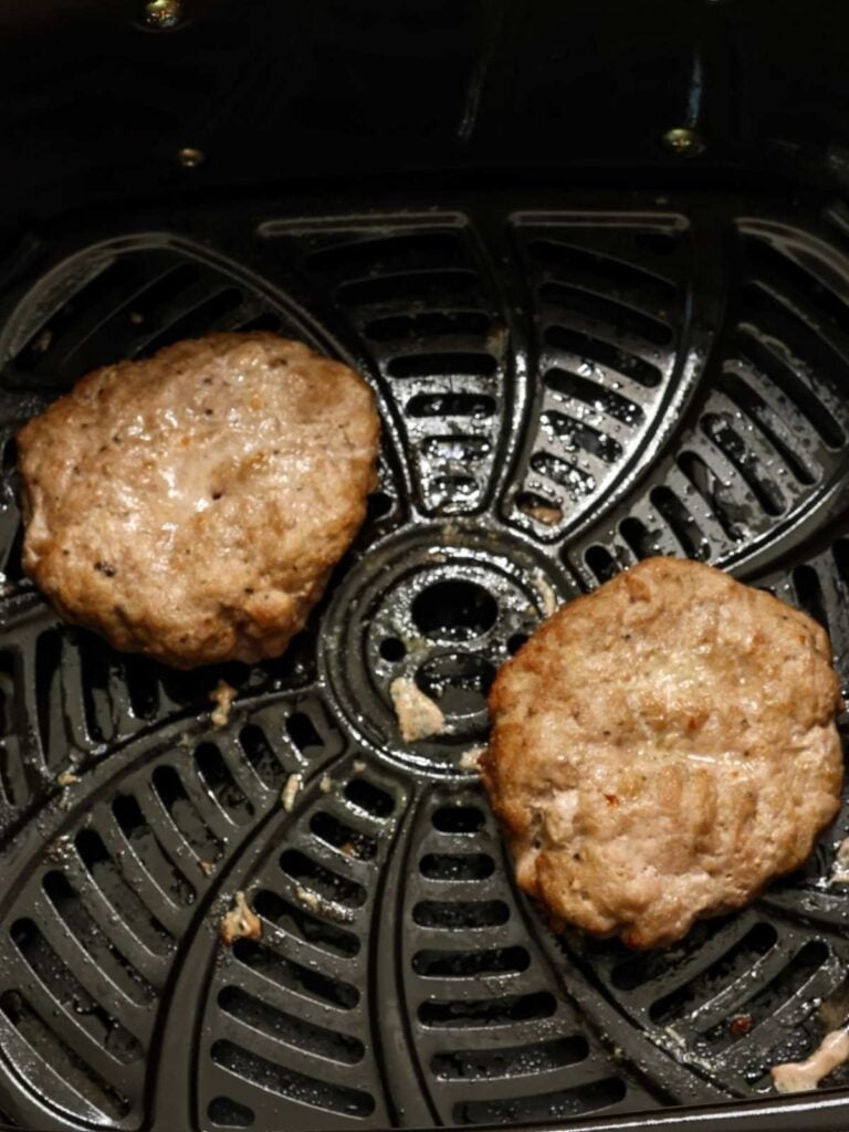 Two ground turkey burger patties in an air fryer basket after they've been air fried.