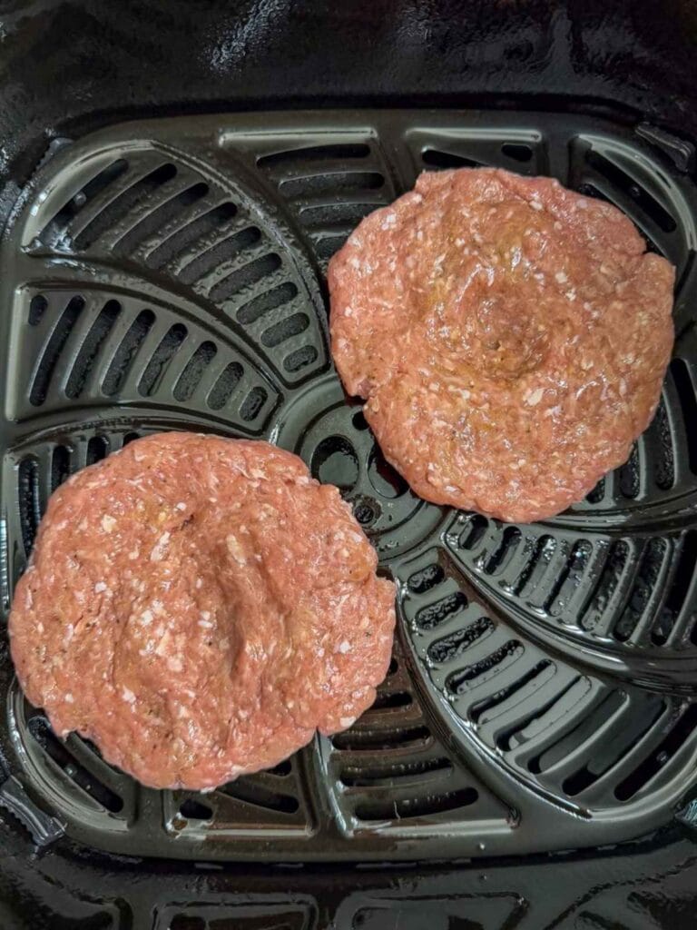 Two uncooked turkey burger patties in an air fryer basket.
